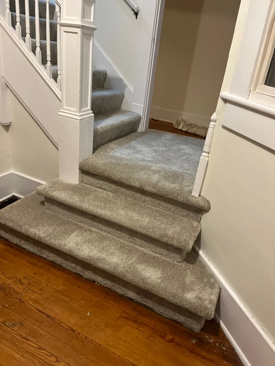 Carpeted staircase with white banisters meeting a hardwood landing